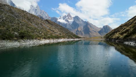 a stunning low-altitude aerial shot flies over a calm alpine lake on the huayhuash trek in peru, capturing the perfect mirror reflection of the snow-capped andes mountains