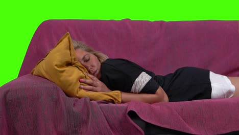 A blonde woman lies down, in slow motion, on the sofa, over a green screen
