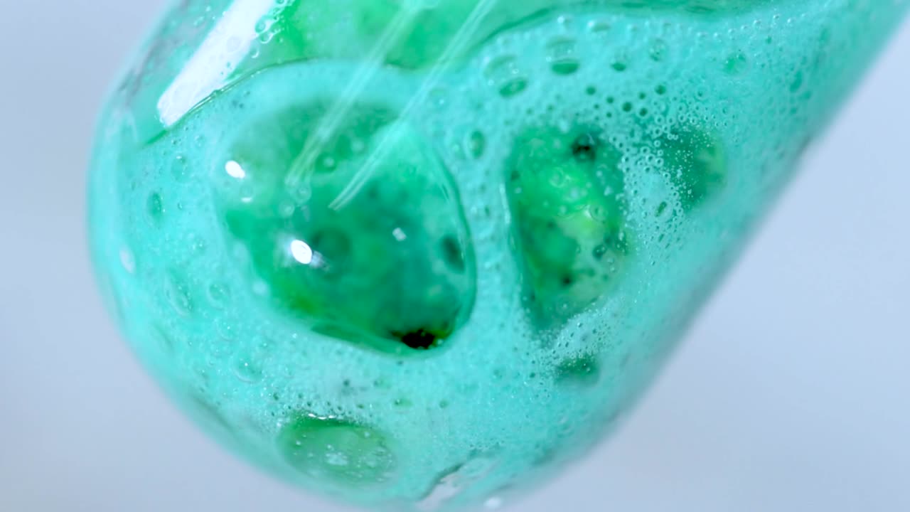 Detailed view of green bubbles forming and expanding in a test tube during a chemical reaction.