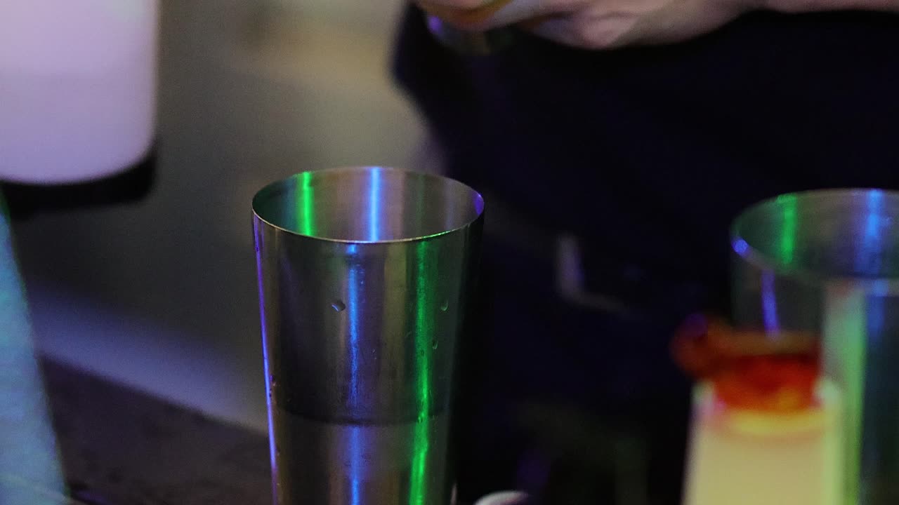 Il barista versa e mescola gli ingredienti di un drink in uno shaker sotto luci al neon colorate, vista ravvicinata