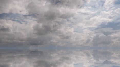 futuristic background consisting of time lapse clip of white fluffy clouds over blue sky and their reflection, video loop