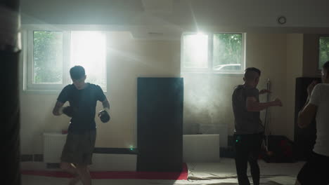 male boxers execute proper punching technique imitating equipment and punching bags in dark gym. group training session. improved strength and endurance