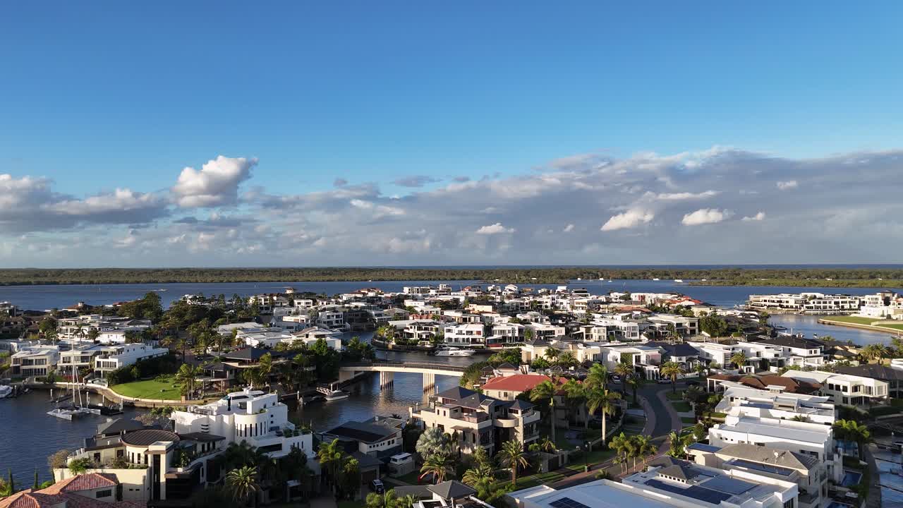Drone footage captures scenic waterfront homes and canals under clear skies in Gold Coast, Australia, with vibrant lighting and serene atmosphere