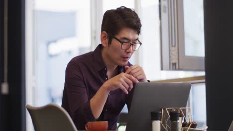 Hombre-Asiático-Haciendo-Una-Videollamada-En-Una-Computadora-Portátil-Mientras-Está-Sentado-En-Un-Café