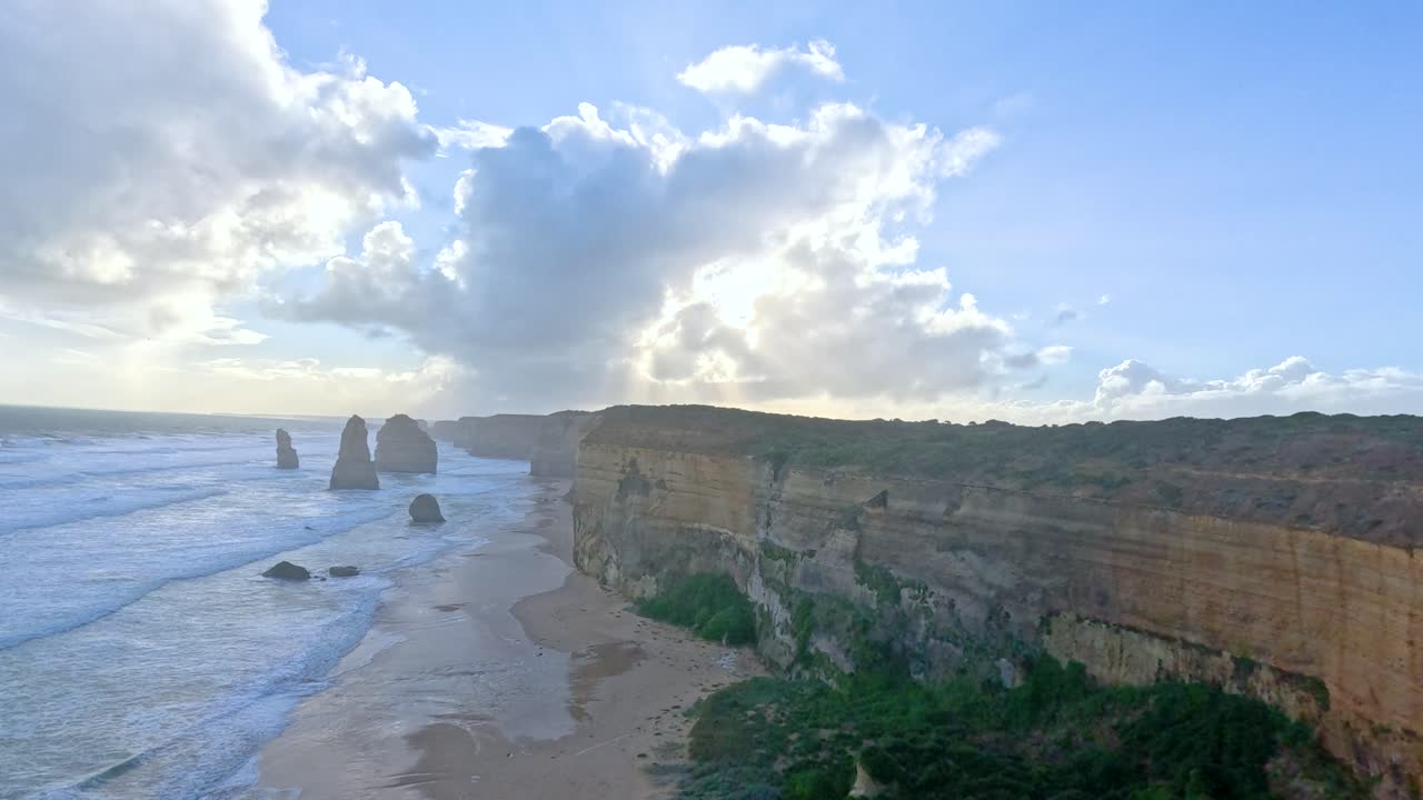 las imágenes aéreas capturan las impresionantes formaciones rocosas de los doce apóstoles a lo largo de la gran carretera del océano de australia al amanecer, mostrando dramáticos acantilados y olas oceánicas.
