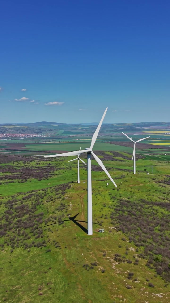 Turbine eoliche su colline sotto un cielo blu di giorno in una zona rurale.