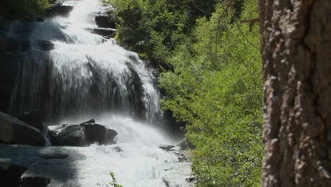 A-moving-shot-past-a-tree-to-reveal-a-beautiful-alpine-waterfall-2