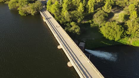 Aerial-birds-eye-shot-of-cyclist-on-bike-crossing-river-by-dam-bridge-in-wilderness-of-Argentina