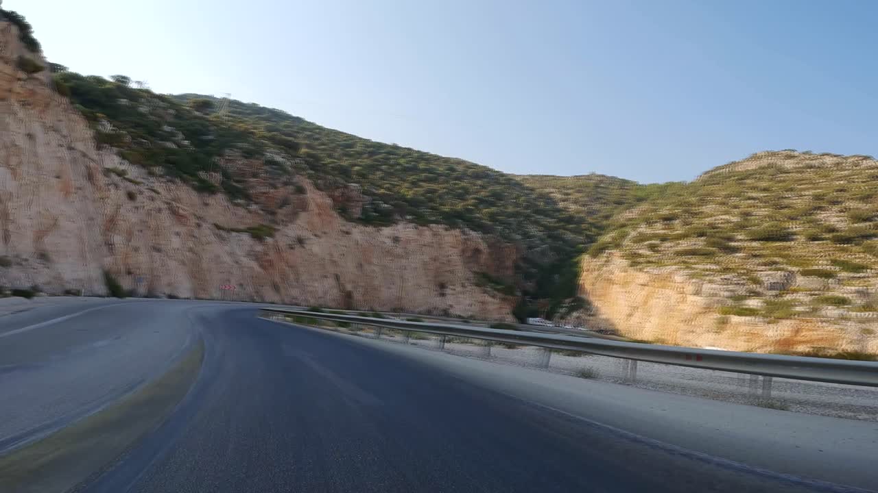 바다와 바위 경사 사이의 터키 도로에서 빠르게 운전하여 산을 볼 수 있습니다.