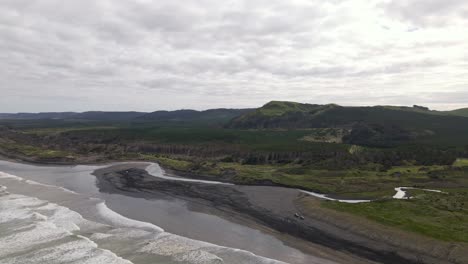 two cars parked on a black sand beach where strong currents and waves form the western coastline of new zealand