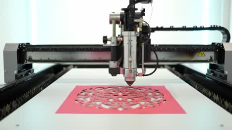 craftsmen operate a laser cutter in a workshop, transforming colored paper into detailed patterns. the precise machinery efficiently carves beautiful designs for various projects.