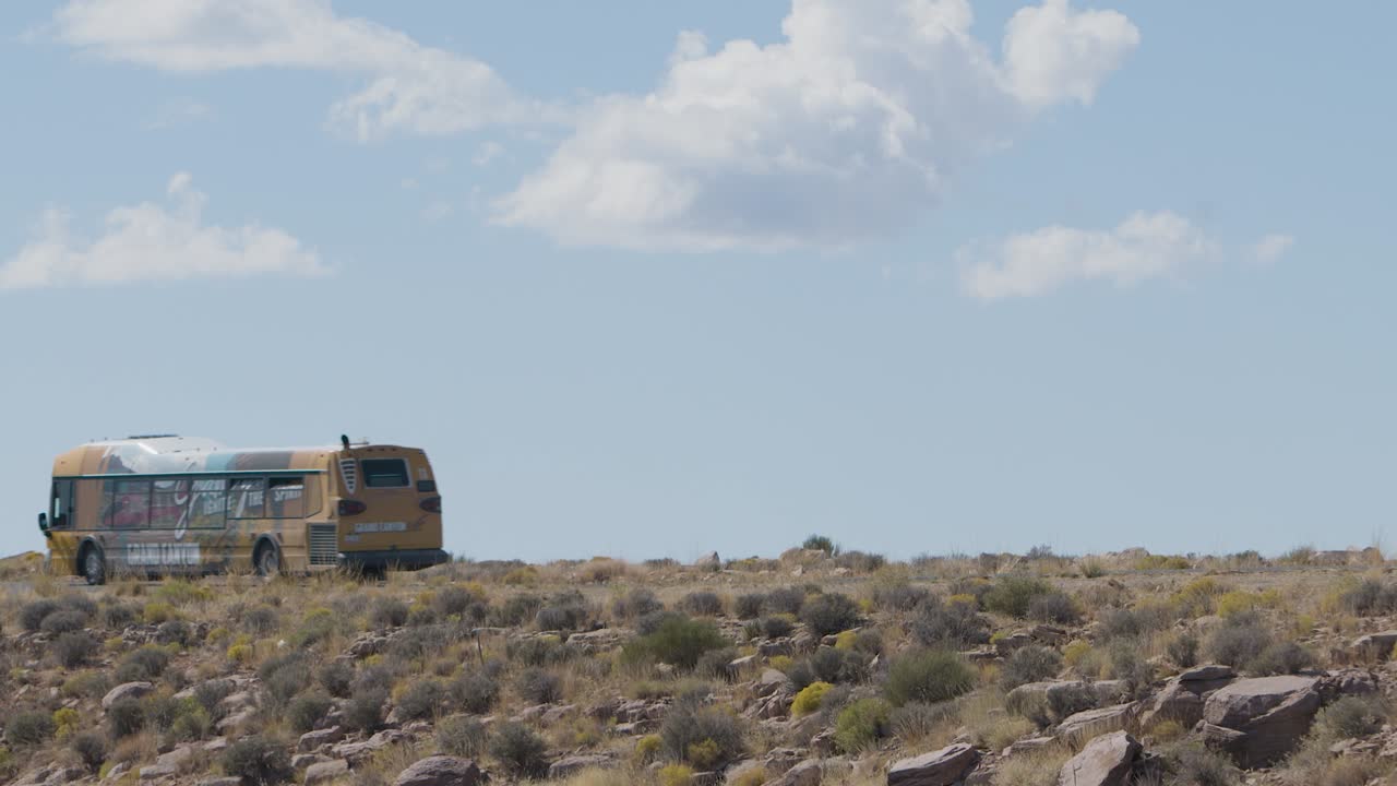 A Grand Canyon Tour Bus passes by and drives off out of frame.