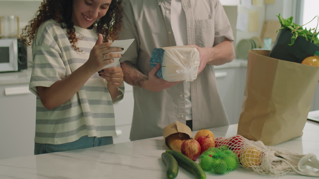 Young Couple Checking Groceries and Reading Receipt at Home