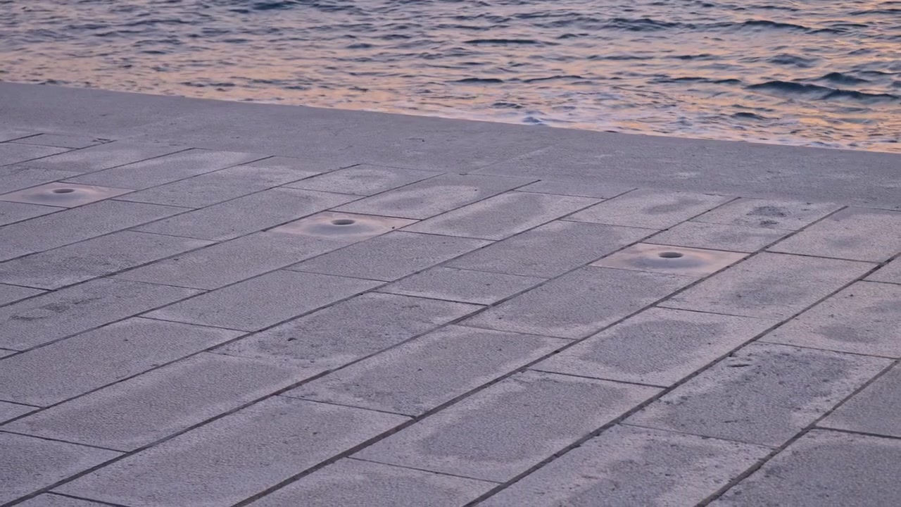 A smooth right pan showing the detail of the acoustic openings at the Sea Organ (Morske orgulje). The footage captures the marble steps where waves create music, located on the Zadar waterfront