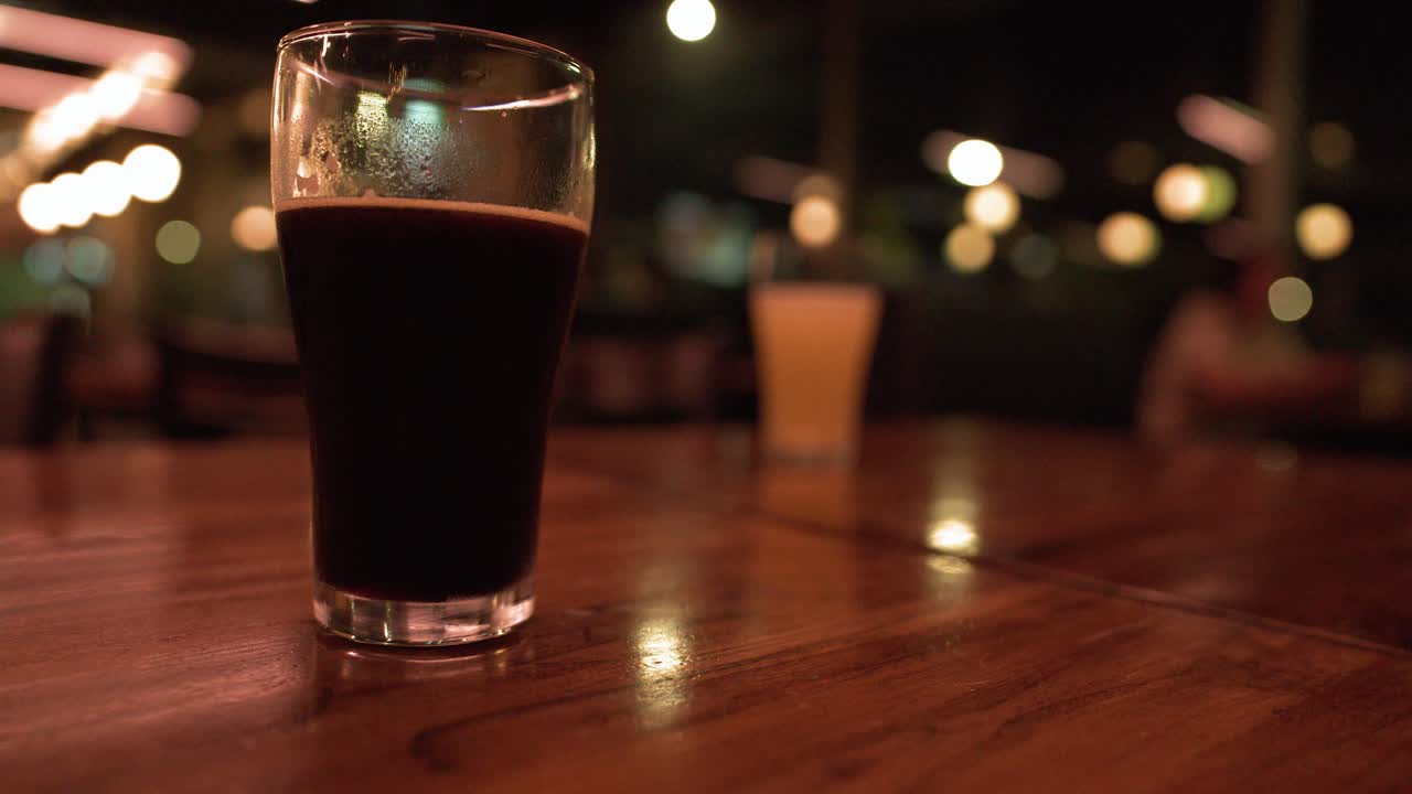 Un primo piano di un bicchiere di birra stout scura su un tavolo di legno lucido