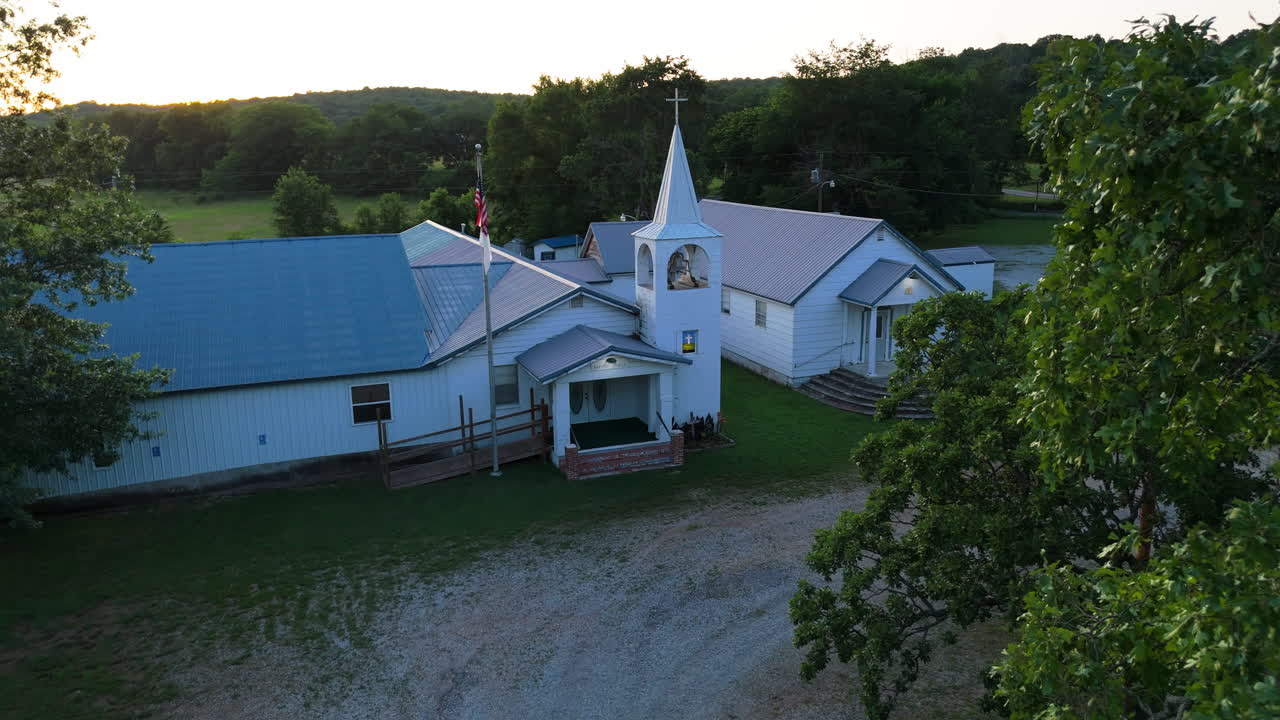 Drone flying through trees to reveal rural America church at sunset. Establishing view of religious building in countryside