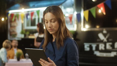 Portrait-Of-Middle-Aged-Beautiful-Woman-Using-Tablet-Device-Outdoors-Truck-Bar-At-Fair