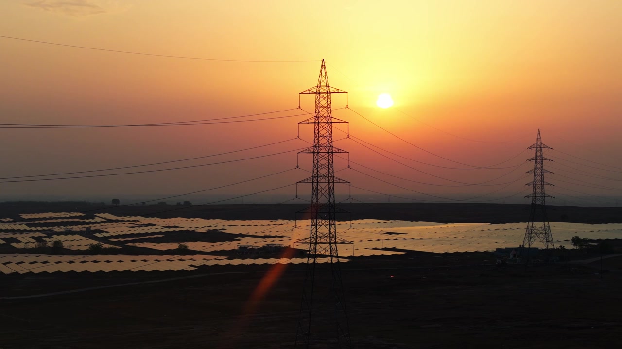 Premium cinematic drone footage tracking right over a vast solar power plant at sunset with transmission towers, showcasing renewable energy, sustainability, and modern energy infrastructure.