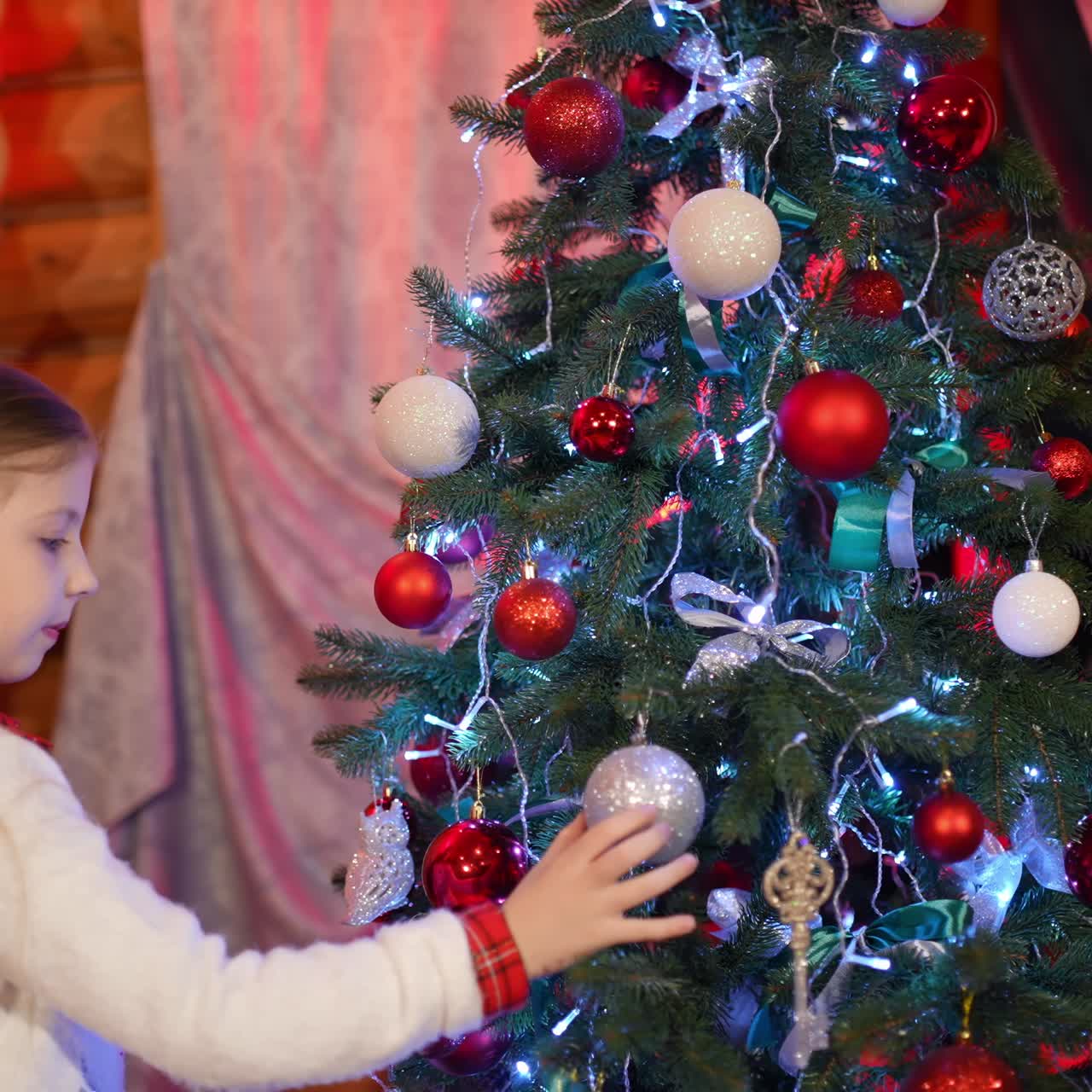 Little girl preparing for Christmas in cosy house. Beautiful child decorating Christmas tree. New Year celebration concept