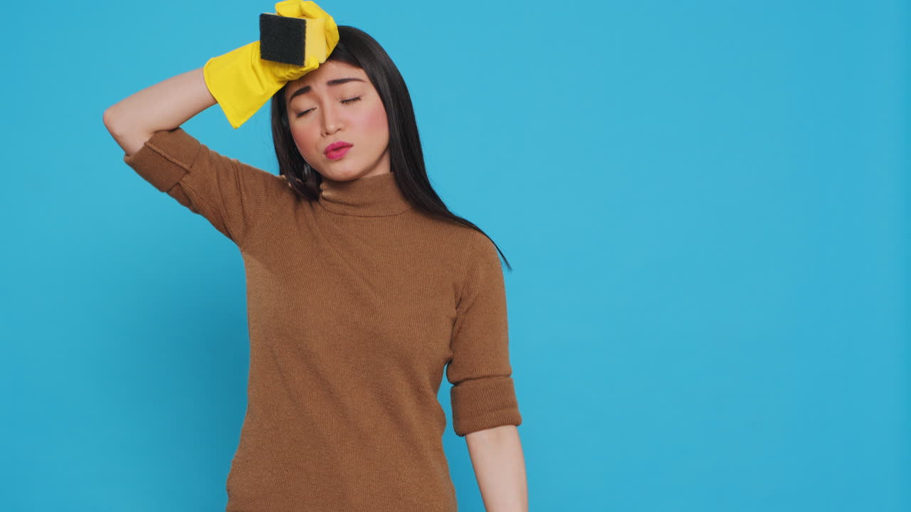 Overwhelmed maid standing in studio over blue background doing intensive cleaning using chemical detergent spray