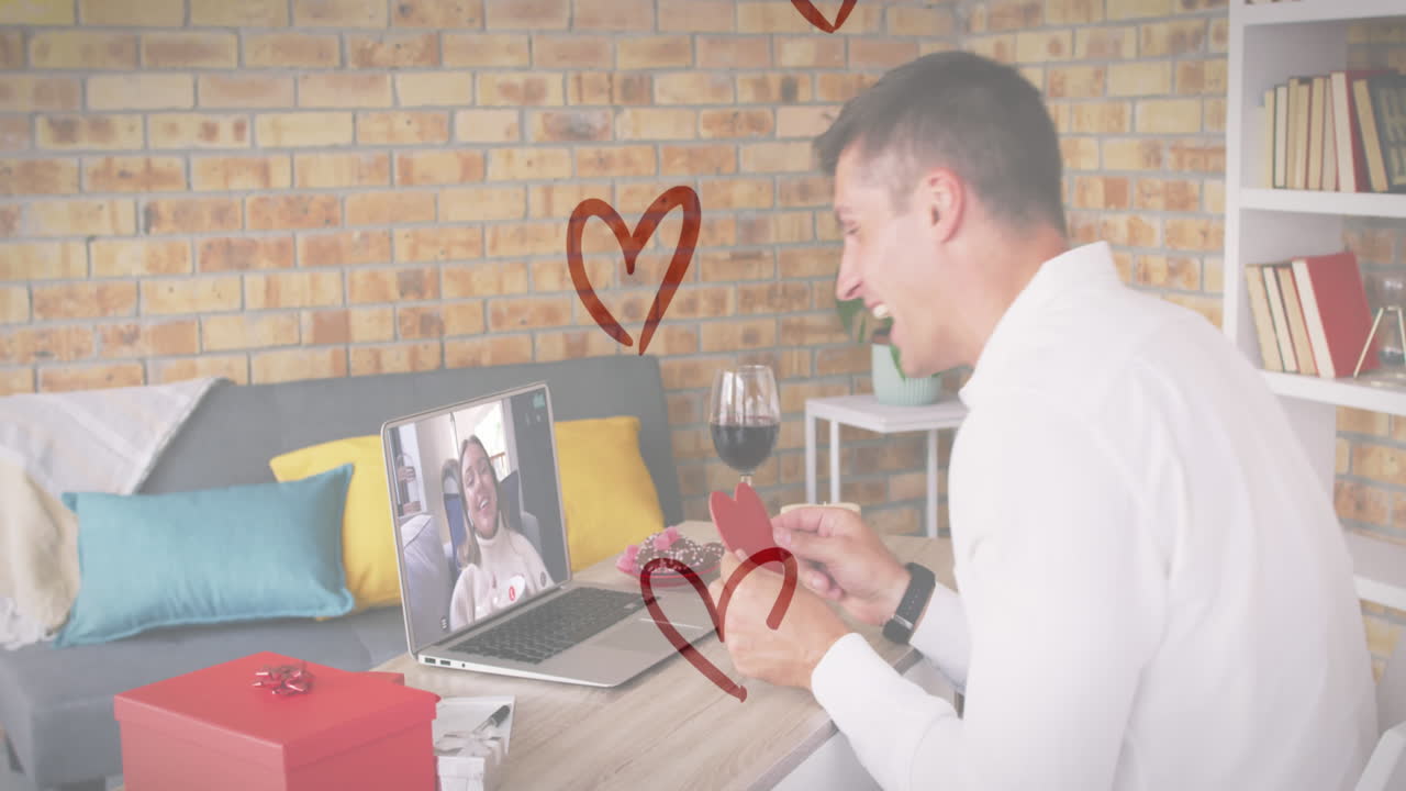 ノートパソコンでビデオコールをしている間 ⁇ ハート形のプラカードを握っている白人男性の上のハートアイコン