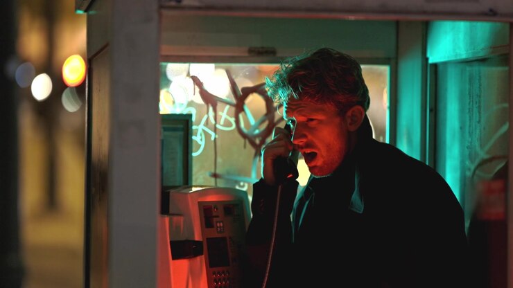 Un uomo elegante parla al telefono in stile noir all'interno di una cabina illuminata da luci al neon