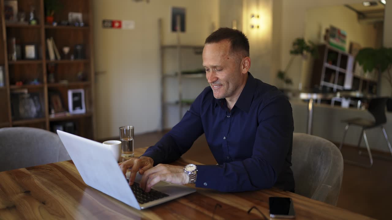 Smiling businessman working on laptop computer at home office. Male professional typing on laptop keyboard at office workplace