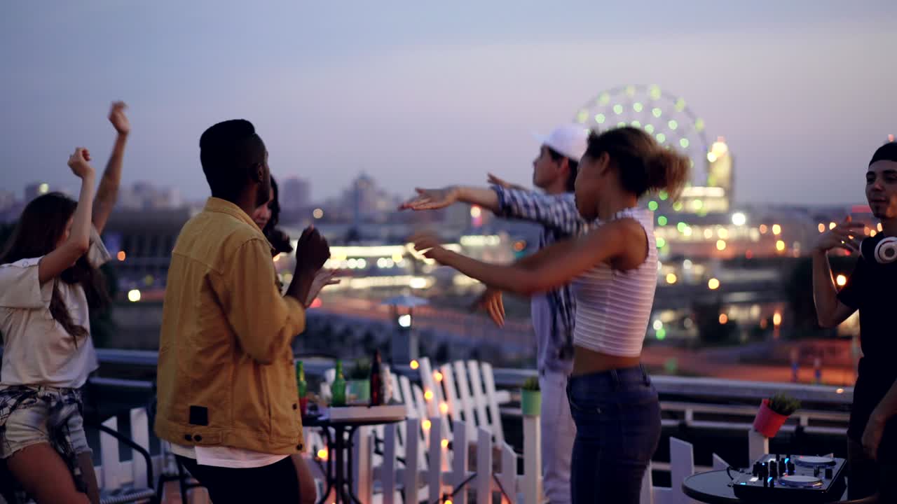 즐거운 젊은이들이 지붕에서 파티를 하고 춤을 추고 웃고있는 동안 dj는 쾌활한 젊은이가 서 장비와 무선 헤드폰을 사용하고 있습니다.