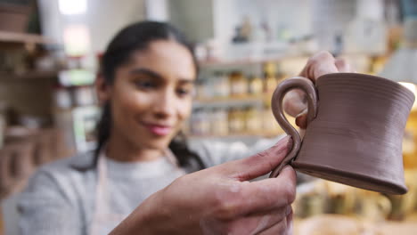 mujer africana americana alfarera atando el mango a la taza en el estudio de cerámica