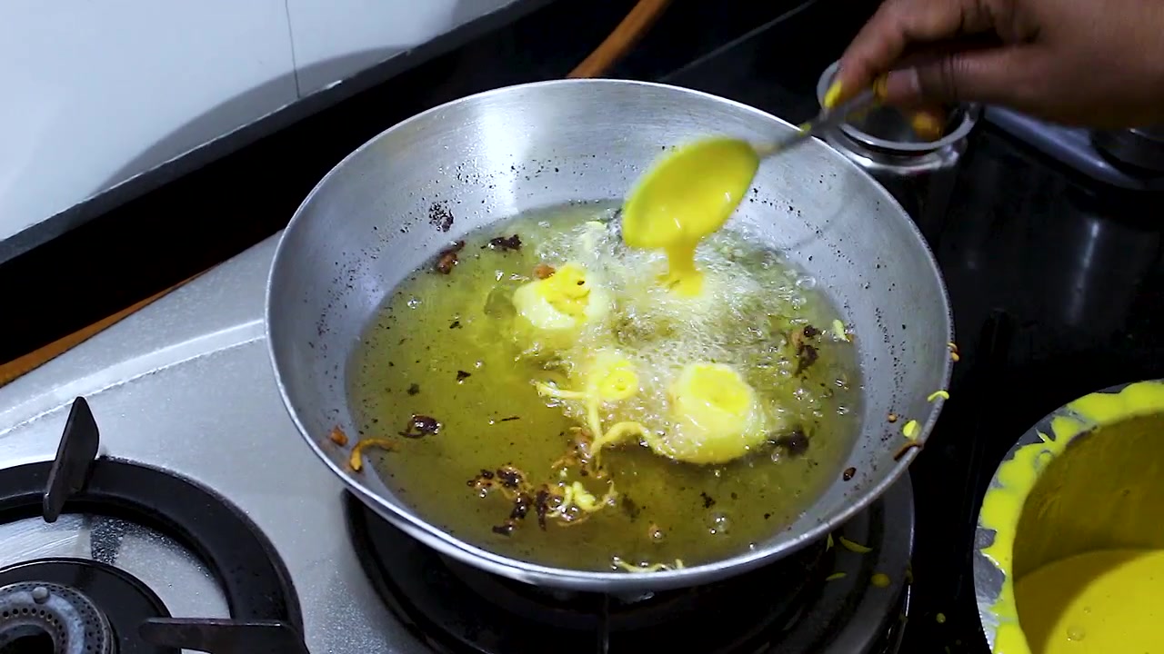 Close-up of batata vada being fried in hot oil during preparation. Perfect for Indian cuisine, street food, cooking tutorials, snack production, and homemade recipe content.