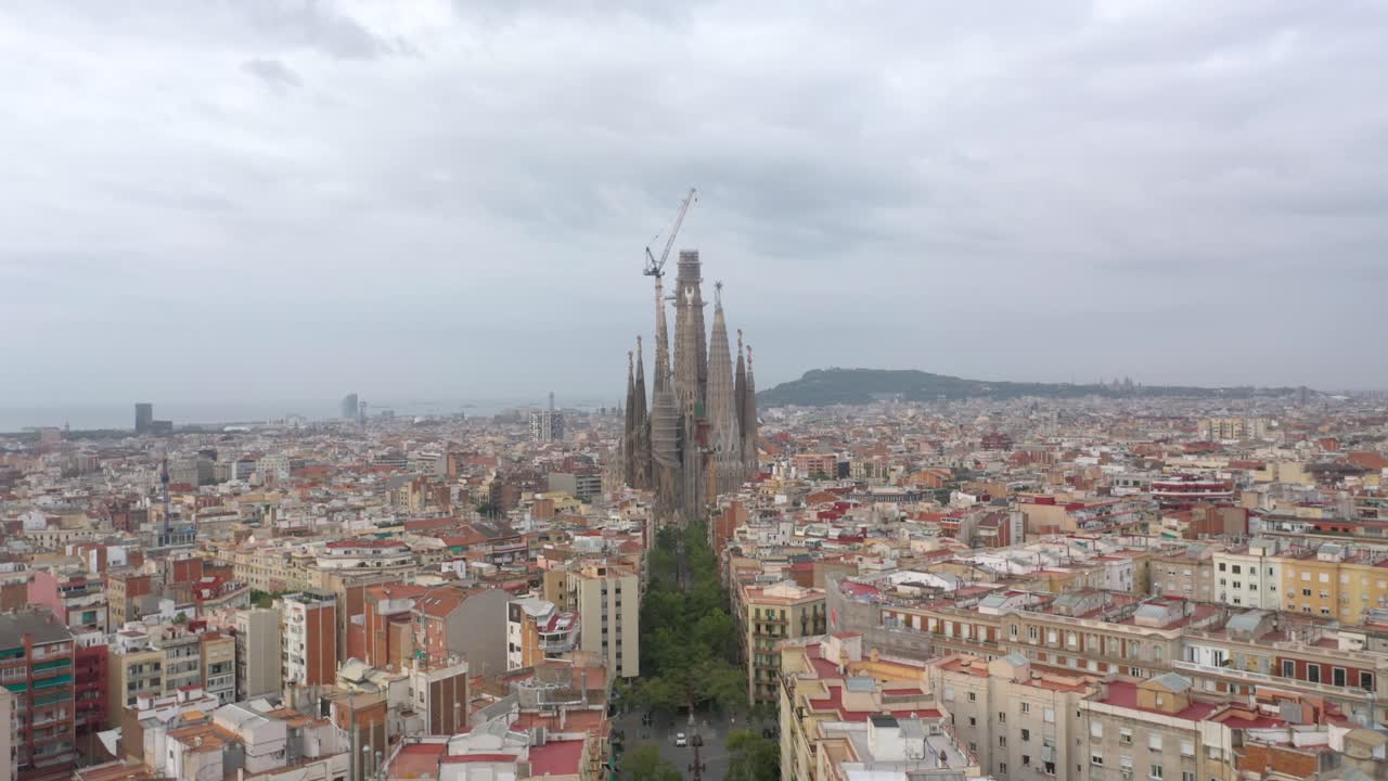 Amazing aerial view descending over the Sagrada Familia in Barcelona capturing the iconic basilica with the city skyline and Mediterranean beach stretching along the horizon