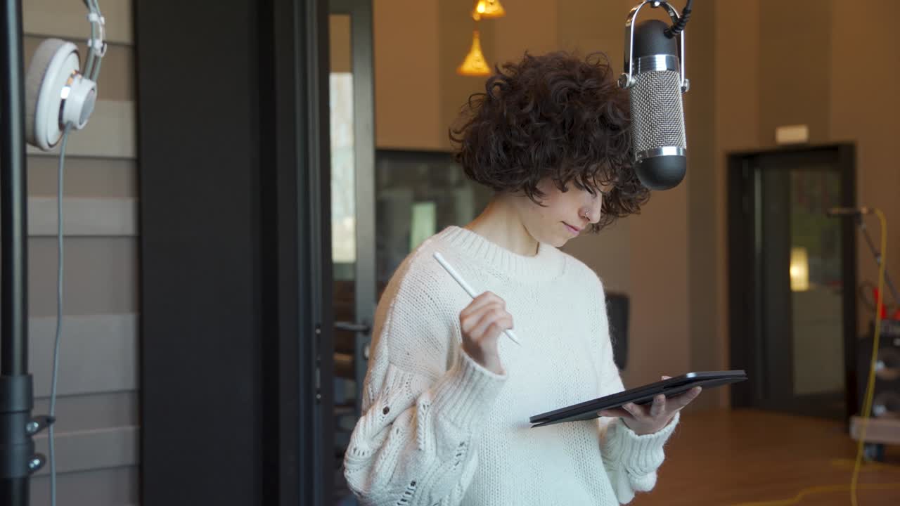 Young woman with curly hair writing and drawing with a tablet in a music studio