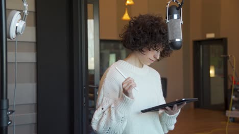 mujer joven con cabello rizado escribiendo y dibujando con una tableta en un estudio de música