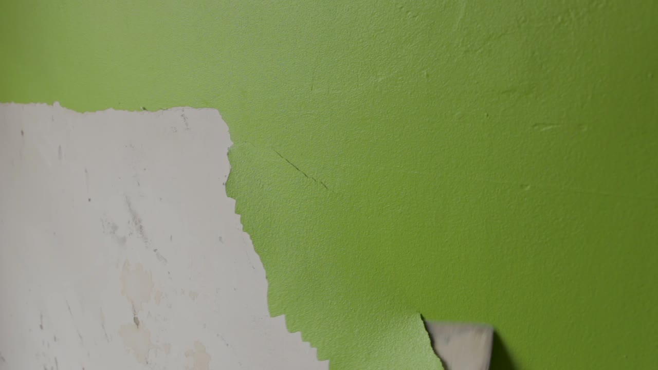 toma fija de un hombre raspando pintura verde de una pared.