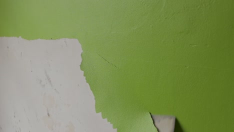 steady shot of a man scraping off green paint from a wall