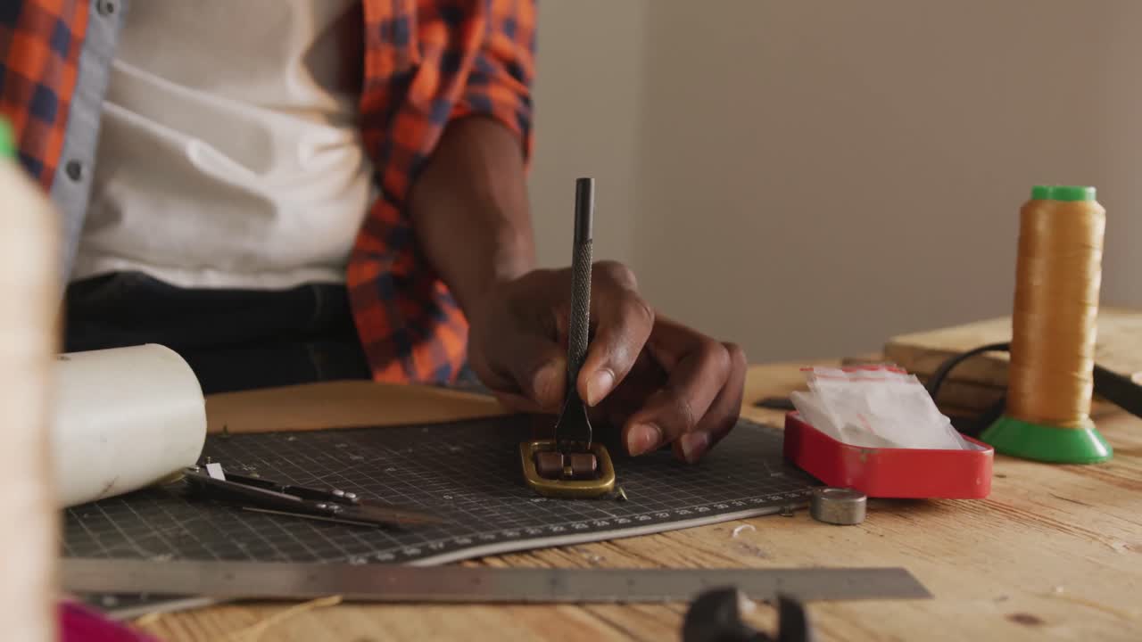 Hands of african american craftsman preparing belt in leather workshop