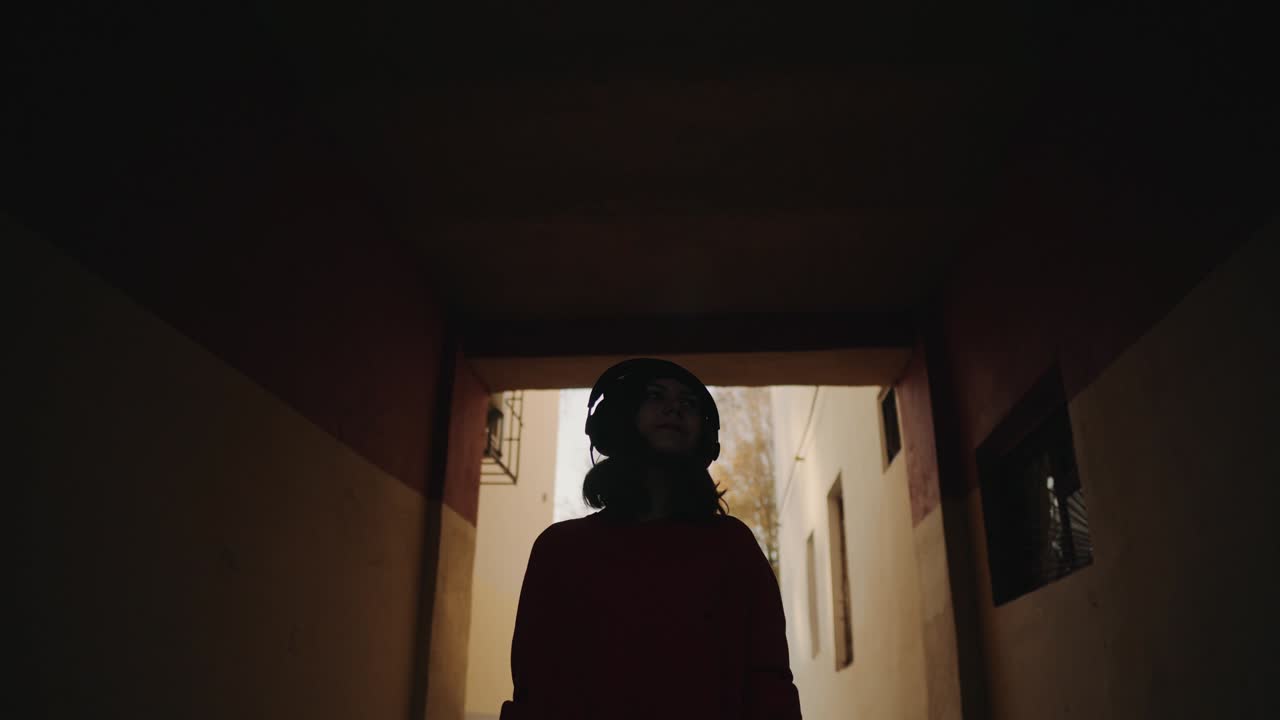 cute young girl walking street between buildings and listening music in headphones, urban style, stylish hipster teen in black hat listen music and smile, orange crazy style