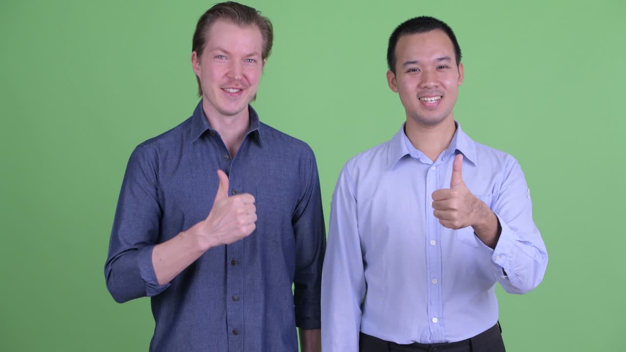 dos hombres de negocios sonriendo y levantando el pulgar contra el fondo del estudio verde