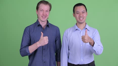 two businessman smiling and giving thumb up against green studio background
