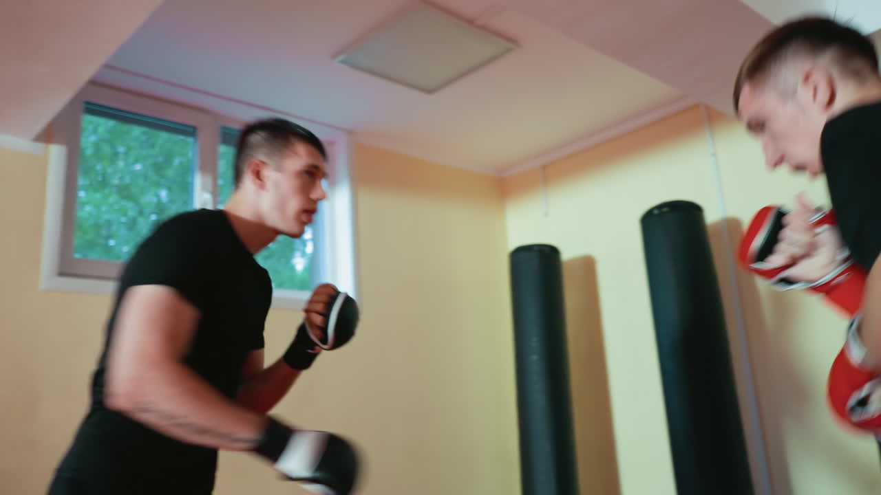 Grapplers engaged in sparring practice inside gym, one defending with red gloves raised, other facing with black gloves, showing combat skill, intensity, focus, endurance, and dynamic martial training