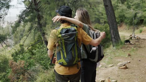 A-happy-couple-backpackers-hiking-by-forest,-exploring-new-places
