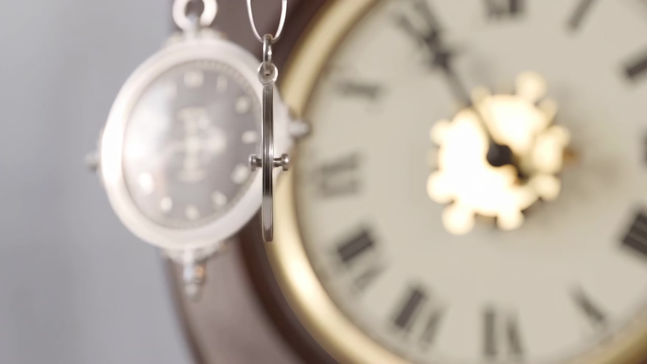 A polished silver pendulum hangs in sharp focus in front of a softly blurred clock face, with warm light, shallow depth of field, and a calm composition