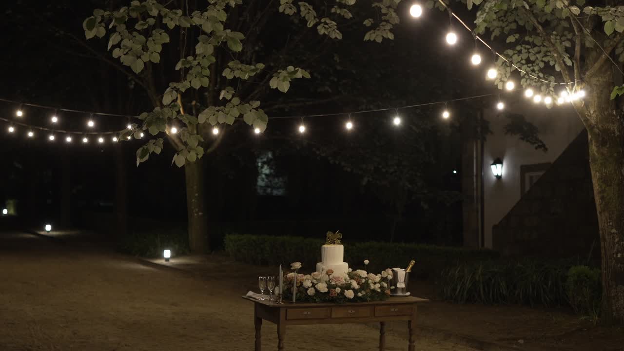 Outdoor wedding setup with string lights and a decorated cake table at night