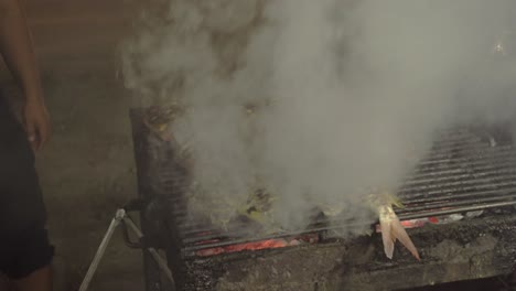 loads of smoke coming up from a charcoal grill full of fish