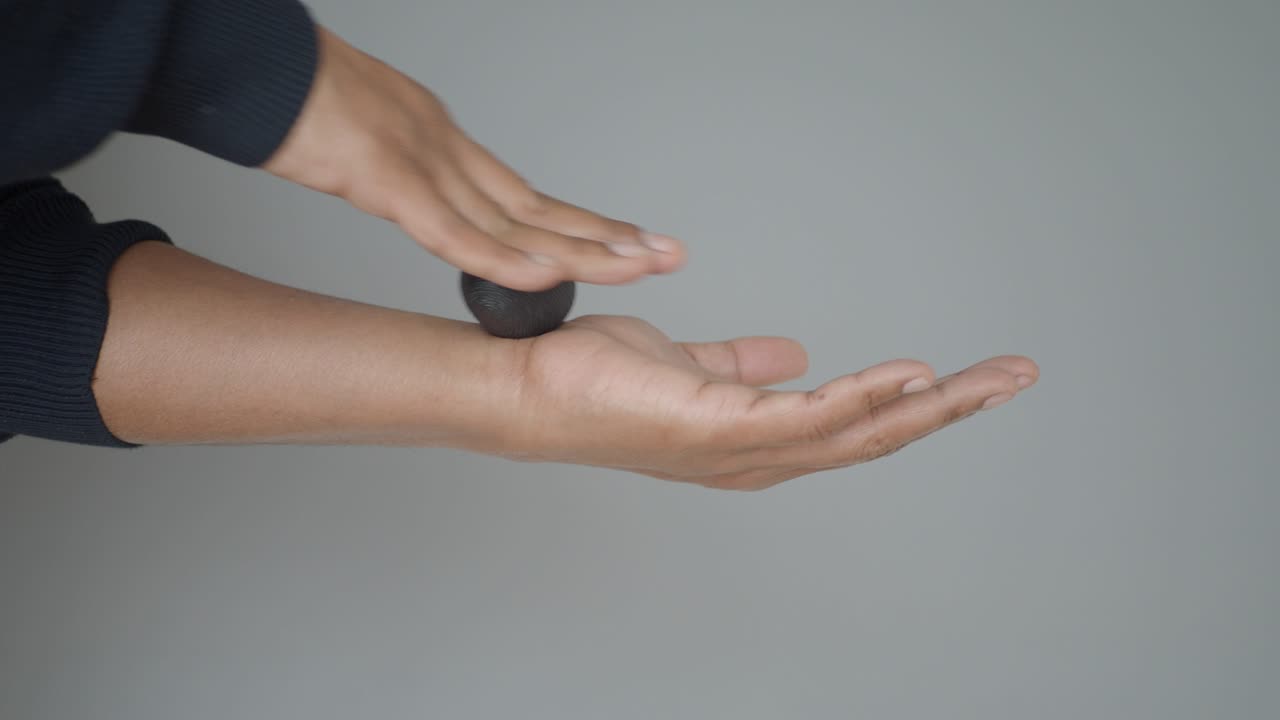 Persona che fa rotolare una piccola palla nera sulla mano per un massaggio