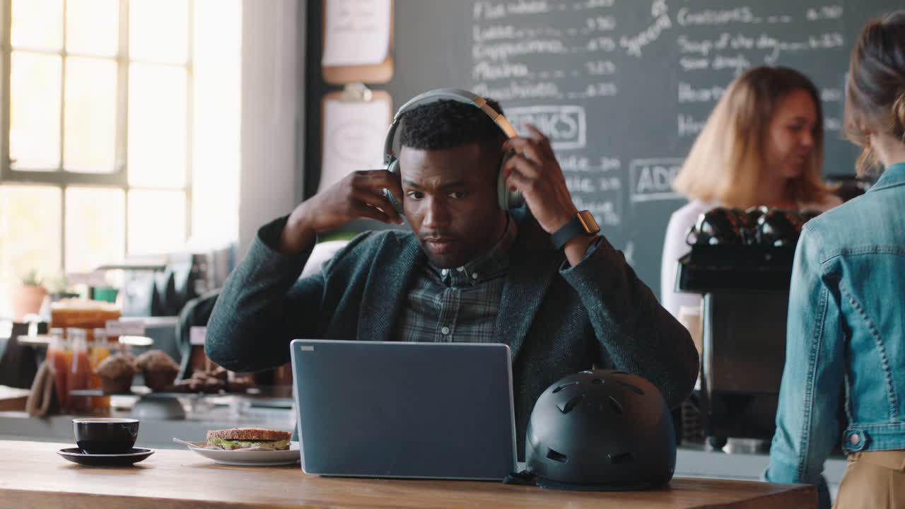 young african american man using laptop in cafe browsing online listening to music wearing headphones enjoying mobile computer technology