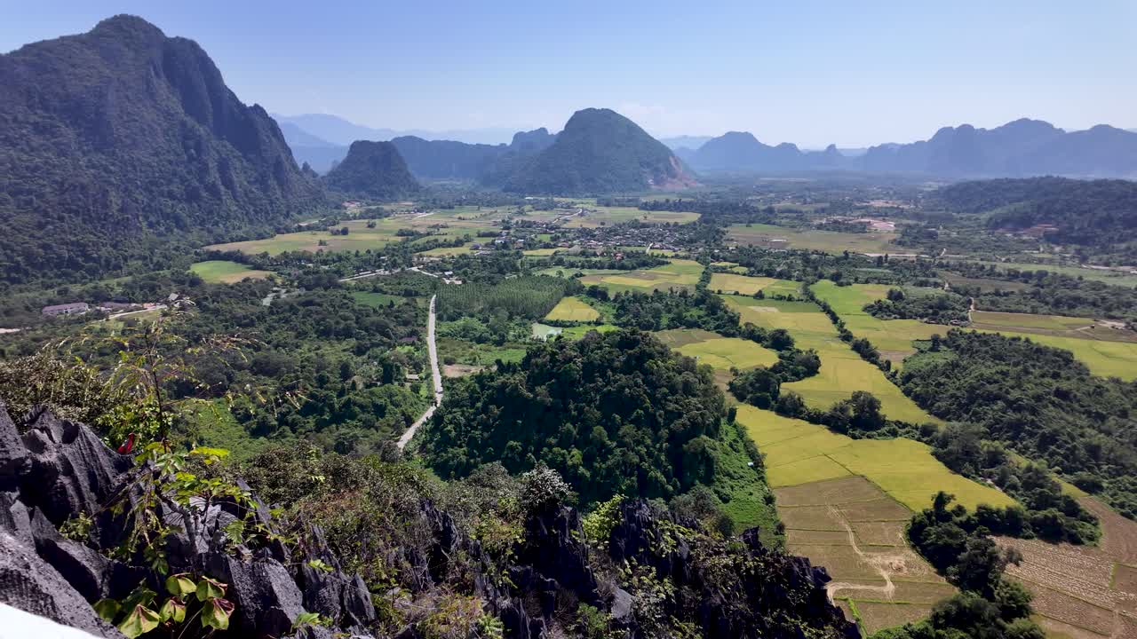 Phong cảnh Vang Vieng ở Lào nhìn từ Điểm Quan Sát Nam Xay, thể hiện những ngọn núi, cánh đồng và cây xanh tươi tốt dưới bầu trời xanh trong. Cảnh quay quét ngang