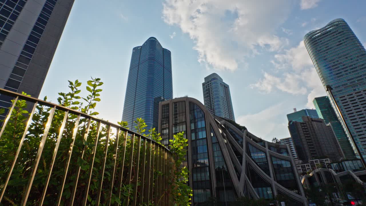 Upward view of impressive modern skyscrapers and unique architecture in Tokyo's Toranomon district. Blue sky and clouds highlight sleek glass and steel structures.