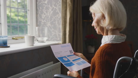 senior woman in wheelchair with energy bill by radiator in cost of living energy crisis