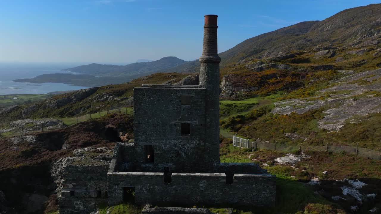 Copper Mine, Allihies, County Cork, Ireland, September 2024. Drone orbits clockwise around historic ruined Engine House chimney on a mountain slope lit by a bright sun on a clear Autumn day.